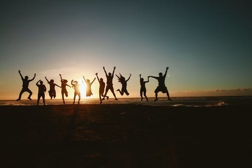 Silhouettes of 11 people jumping on a beach with the ocean and sunset behind them 