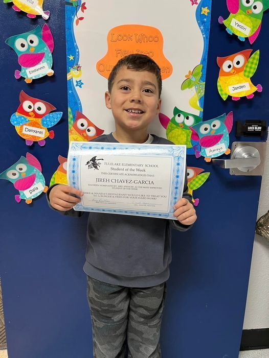 young student holding an award certificate in the school hallway 